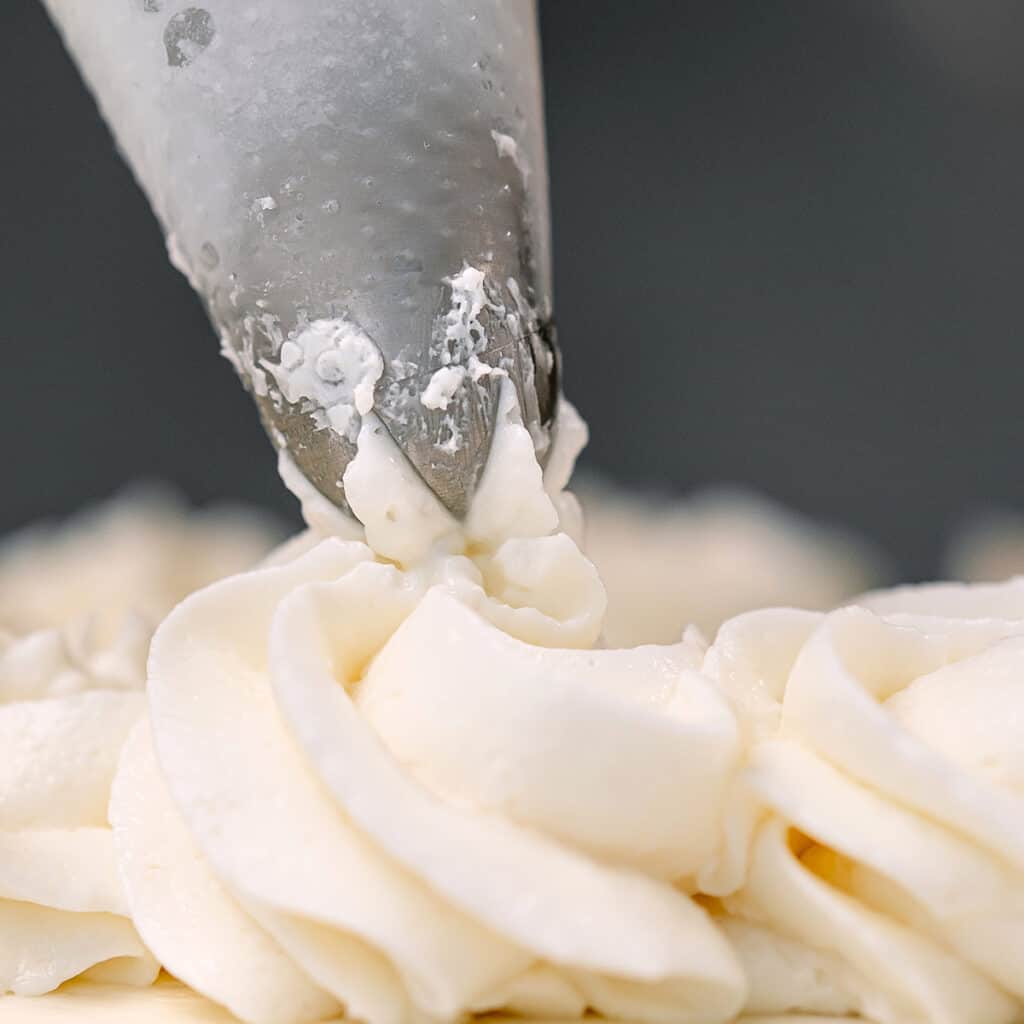A close up image of decorating a pie with piped whipped cream.