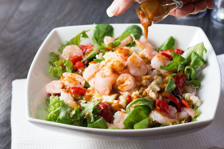 shrimp salad in a white square bowl with dressing being drizzle over it