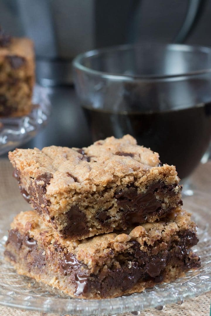 two chocolate chip spiced bars stacked on top of each other on a plate with a cup of coffee in the background