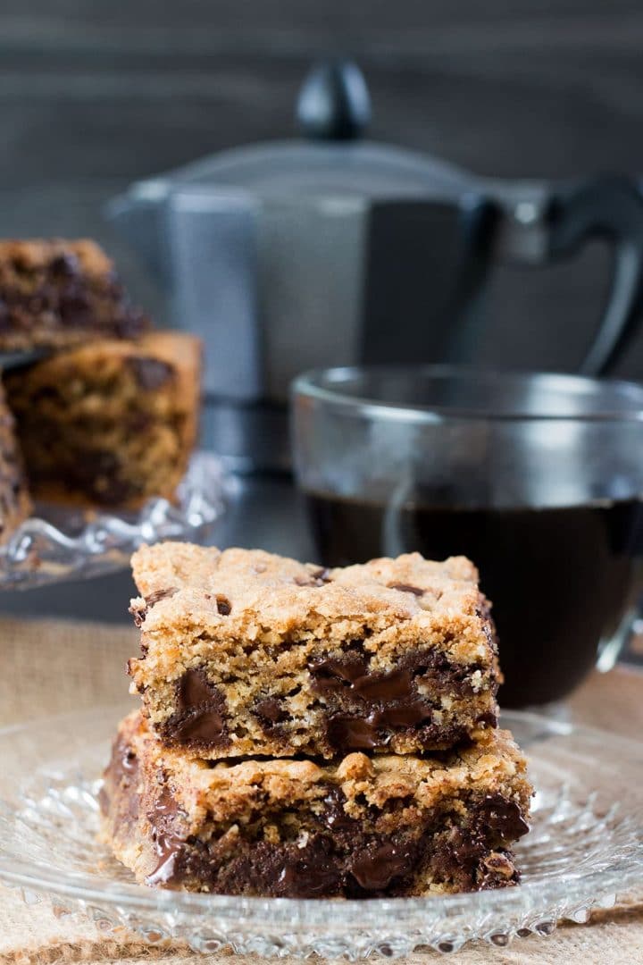 2 Chocolate Chip Spiced Oatmeal Cookie Bars on a crystal plate with a cup of coffee in the background