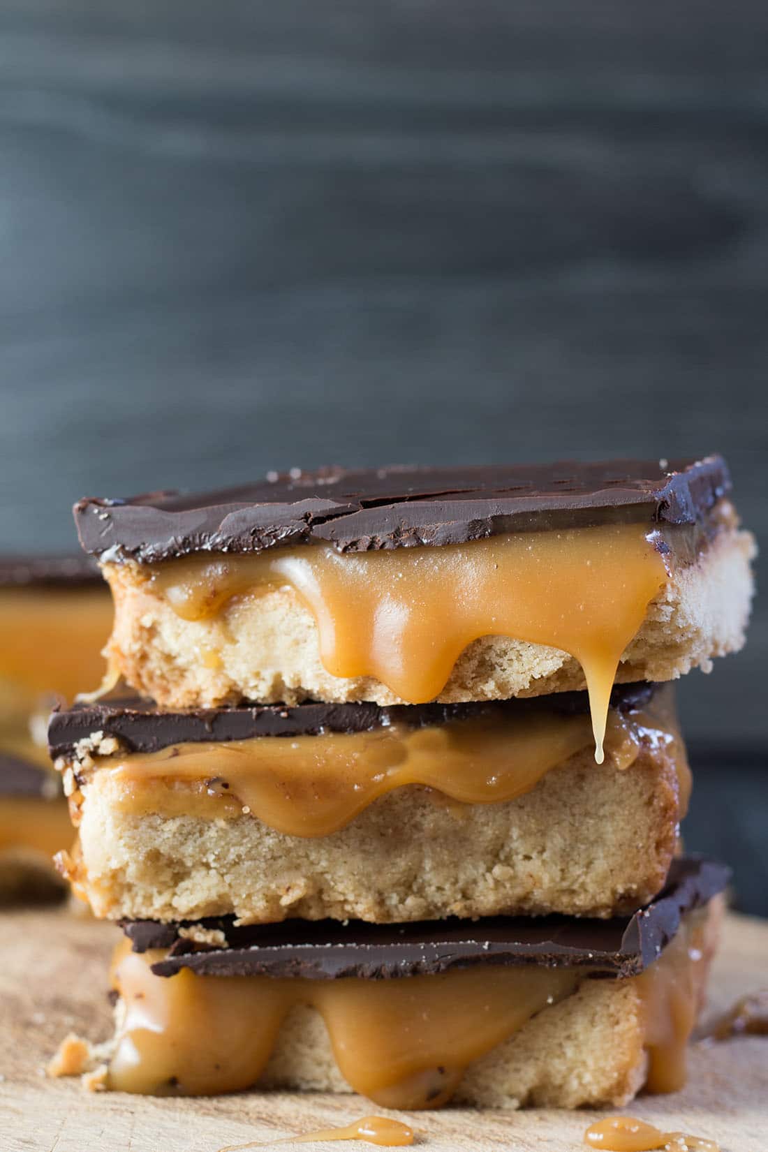 two slices of billionaire shortbread stacked with the caramel from the top slice oozing out to the cutting board below.