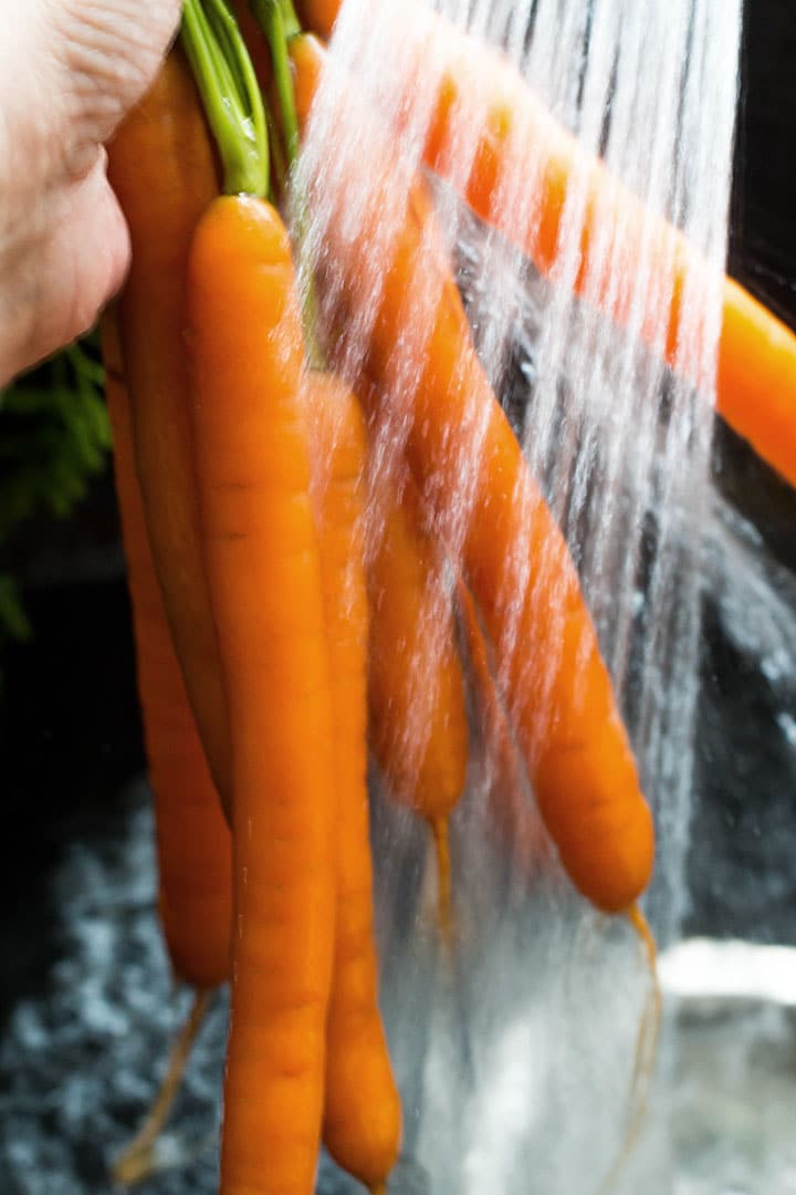 Fresh carrots being washed under running water.