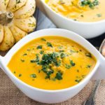 A bowl of winter squash soup with a squash in the background