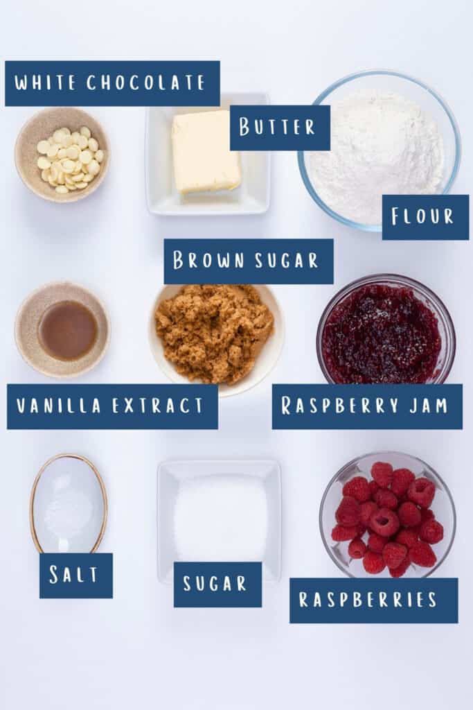 Top-down view of ingredients for a Raspberry Tart, each labeled with text on the image. There are bowls containing white chocolate chips, butter, flour, brown sugar, vanilla extract, raspberry jam, salt, sugar, and fresh raspberries.