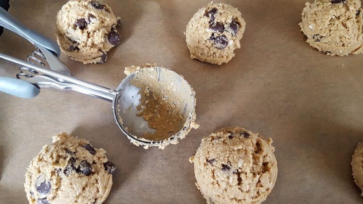 Chocolate Chip Oatmeal Cookie dough scooped on a cookie sheet with a ice cream scoop laying next to them