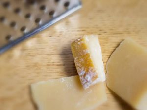 Chunks of Parmesan cheese on a cutting board with the rind in focus