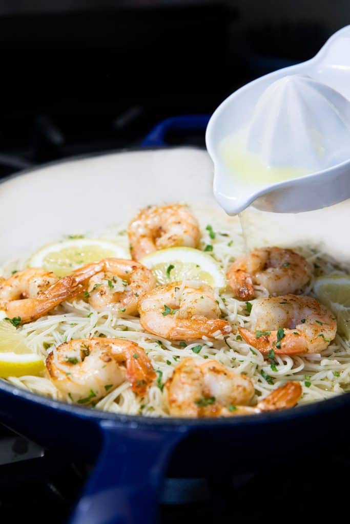 lemon juice being added to the pan with the pasta and shrimp mixture