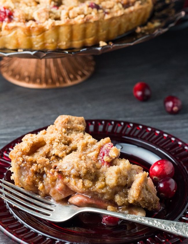 A slice of apple cranberry crumb pie on a red glass plate with a fork next to it