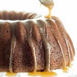 A Brown Sugar Bundt Cake on a glass cake stand being drizzled with Caramel Glaze