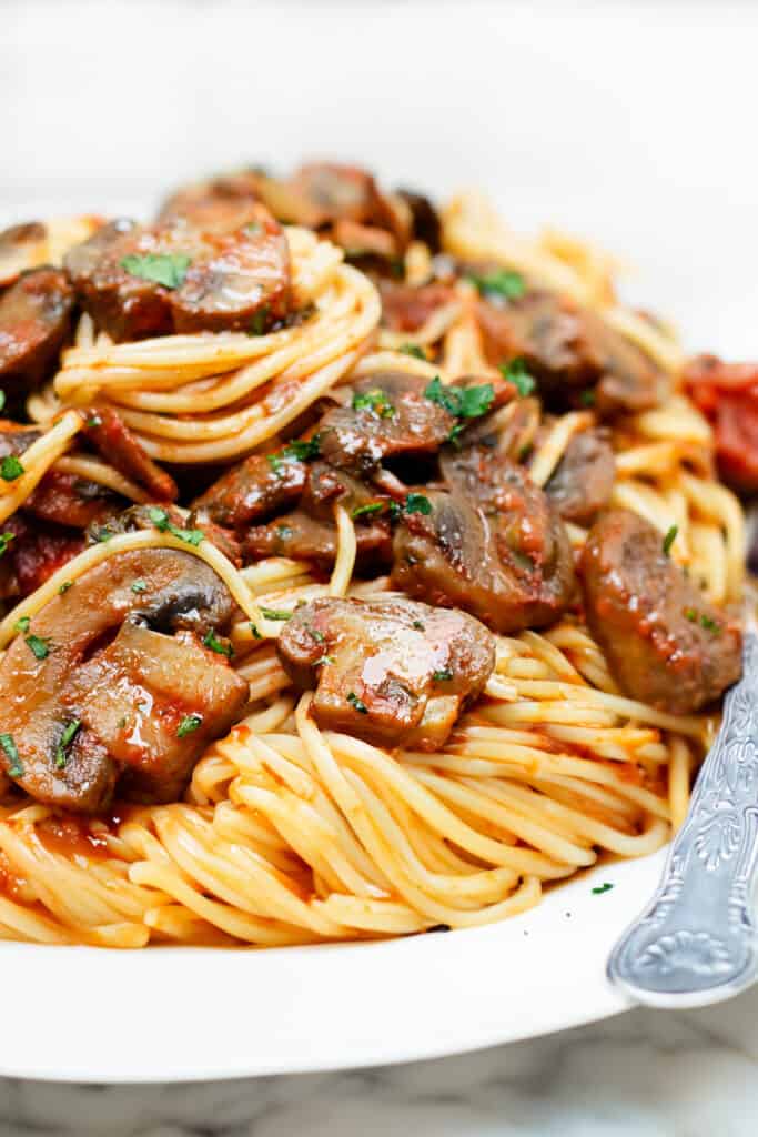 A white plate with a serving of spaghetti topped with a tomato mushroom sauce.