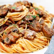 A close up image of plate with a serving of spaghetti topped with a tomato mushroom sauce.