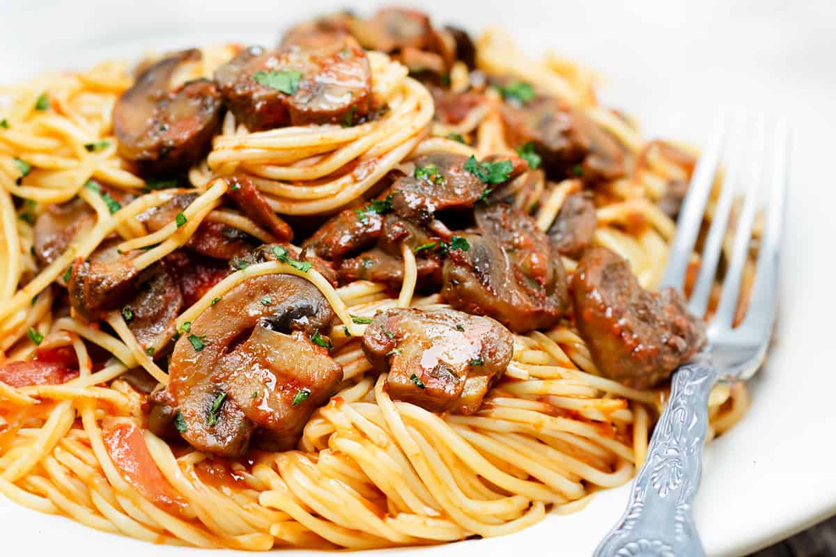 A close up image of plate with a serving of spaghetti topped with a tomato mushroom sauce.