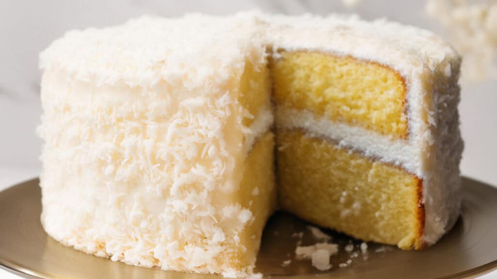 A Coconut Lovers Dream Cake on a bronze plate, showcasing its moist yellow layers and creamy coconut buttercream frosting, all sprinkled with shredded coconut.