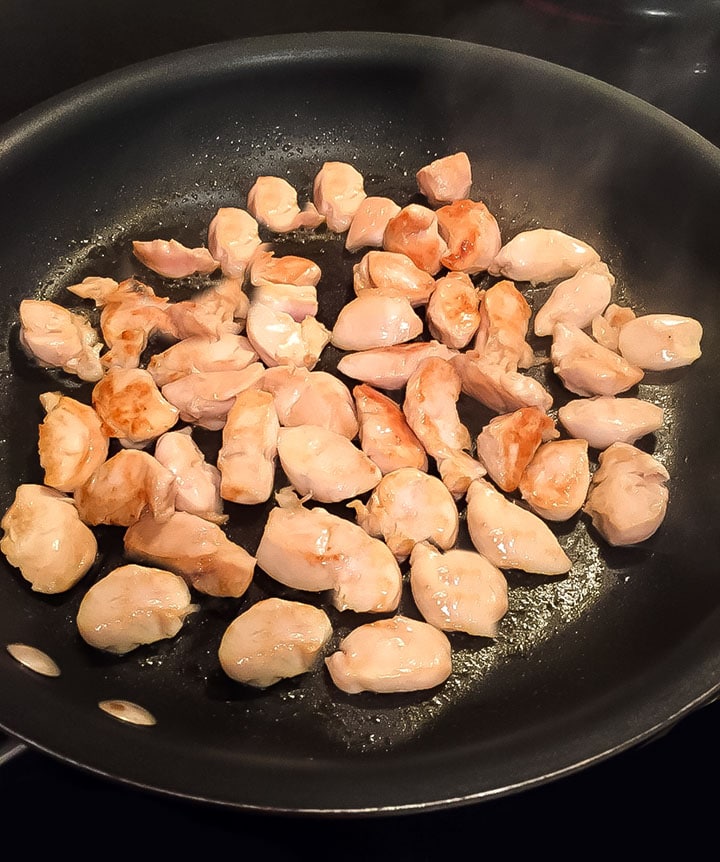 Chicken cut into bite sized pieces browning in a pan.