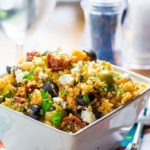 10 Minute Greek Couscous Salad with Feta & Sundried Tomato Dressing piled high in a bowland spinkled with fresh herbs and extra feta