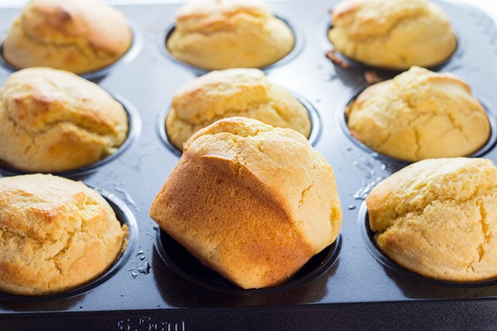 A pan of Easy Homemade Corn Muffins with one out to show the golden exterior