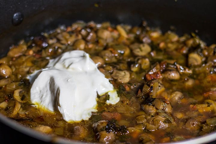 A pan with mushrooms cooking with a dollop of sour cream