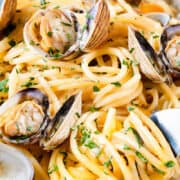 a plate of spaghetti with white clam sauce with clams in the shell and a fork twirling spaghetti