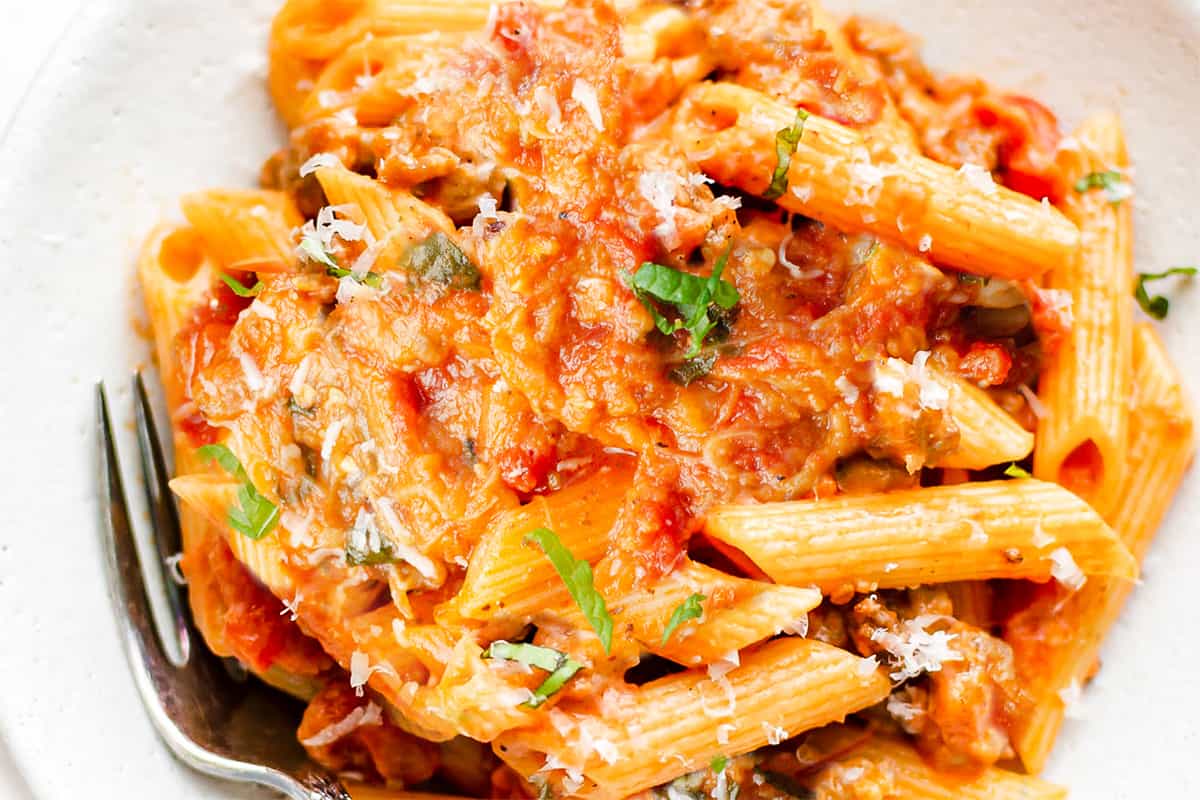 an overhead image of a bowl of pasta alla Norma with a fork and basil leaf