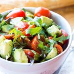 A bowl of bright and colorful tomato avocado salad with some bread in the background.