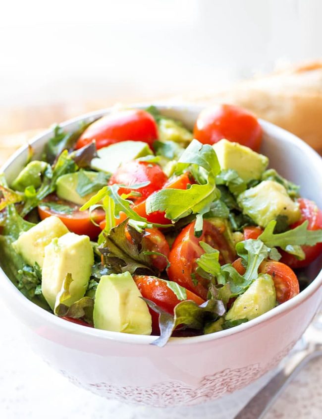 a bowl of the vibrant and colorful tomato avocado salad with some bread in the background