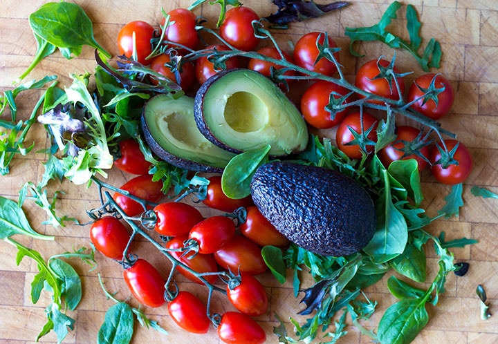 a cutting board covered in cherry tomatoes, still on the vine, avocado and fresh greens