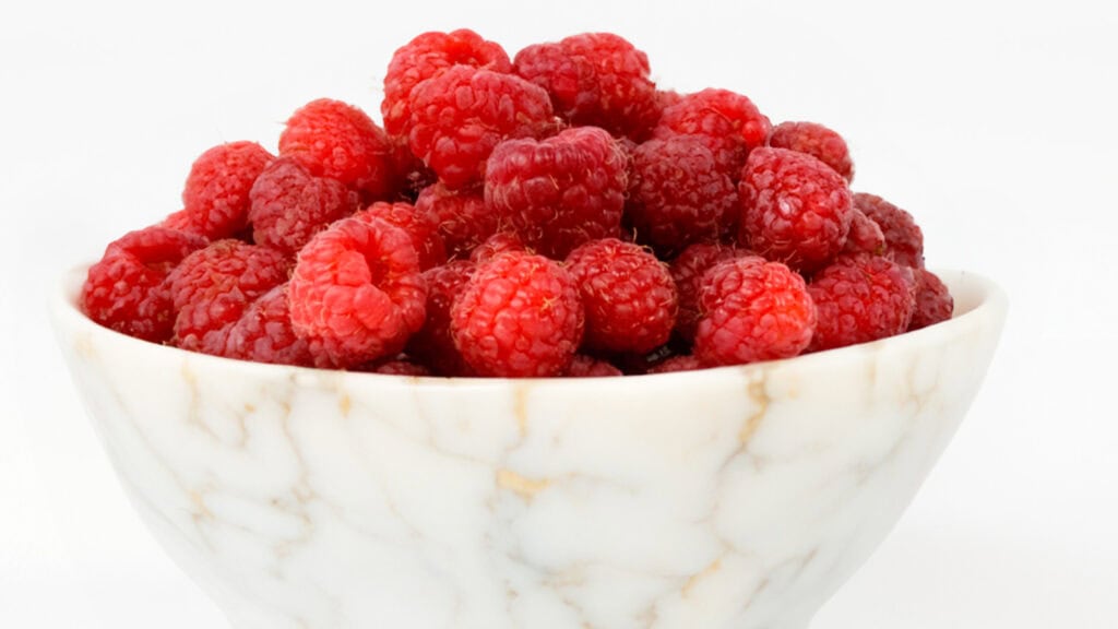 A close up image of a white marble bowl of raspberries.