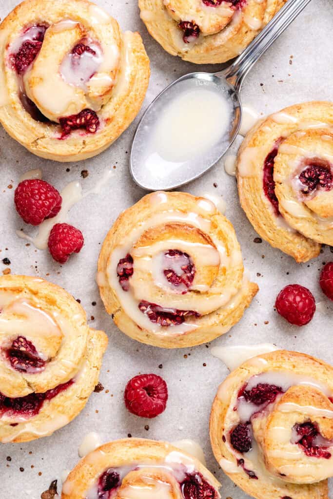 Close-up of raspberry swirled scones with icing on parchment paper, displaying the swirls of dough and berry filling.