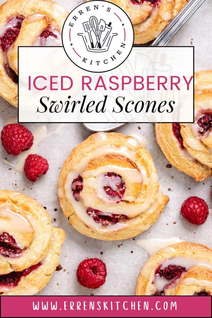 Iced raspberry swirled scones with a glaze on a baking sheet lined with parchment paper. The scones are round and a light golden brown color. There is a bowl of leftover raspberries beside the baking sheet