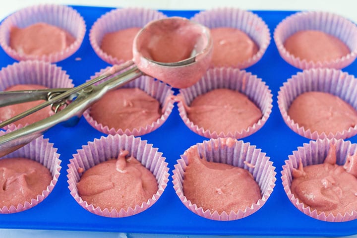 The batter added to the cupcake papers in the bright blue pan