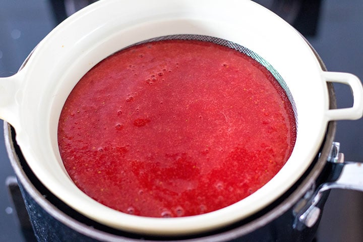 The puree running through a strainer to remove the seeds