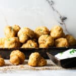 A plate of fried breaded garlic mushrooms next to a bowl of dipping sauce.