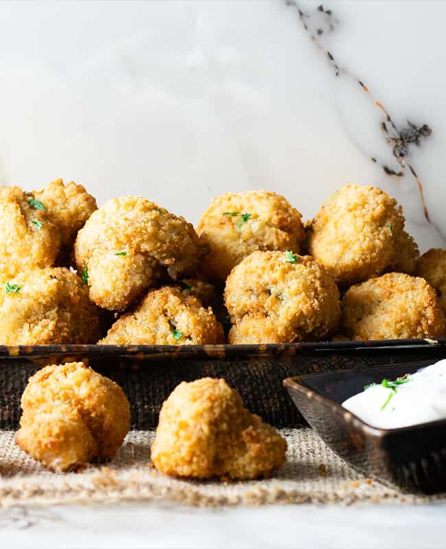 A plate of fried breaded garlic mushrooms next to a bowl of dipping sauce.