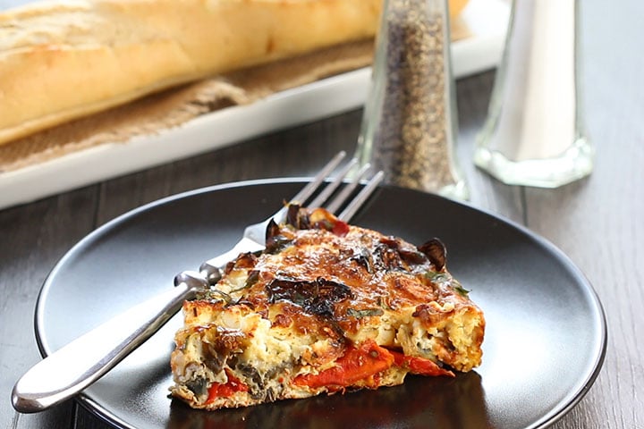 A slice of Baked Eggplant Frittata with Red Onion, Peppers & Feta with bread and salt and pepper in the background