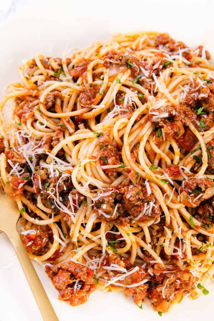 A plate of Quick & Easy Spaghetti Bolognese topped with a rich meat sauce, garnished with grated Parmesan cheese and chopped herbs. A fork rests beside the pasta.