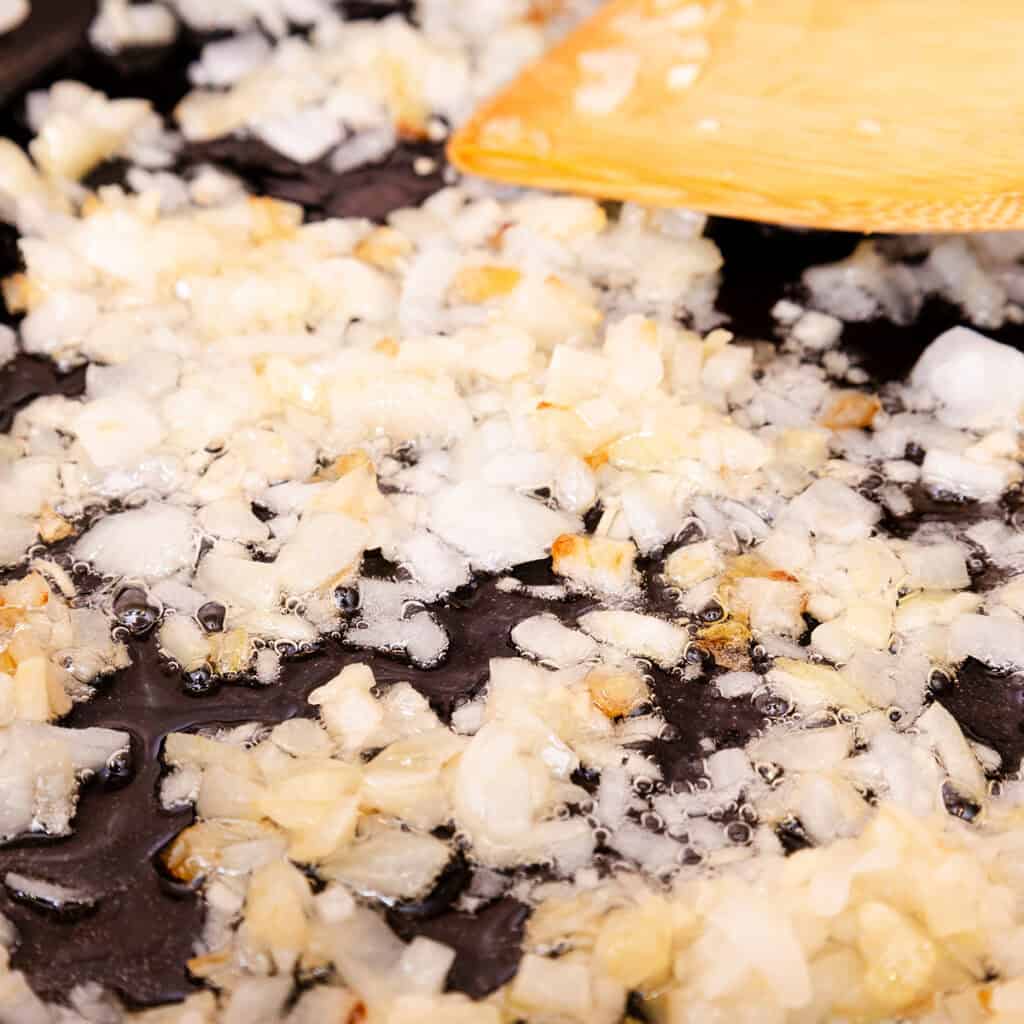 Chopped onions being sautéed in a pan with a wooden spatula, turning golden brown— a quick and easy spaghetti Bolognese essential.