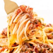 Close-up of a fork twirling Quick & Easy Spaghetti Bolognese, rich in tomato and meat sauce with herbs. The spaghetti is topped with ground meat and bits of tomato, capturing a mouthwatering Italian dish.