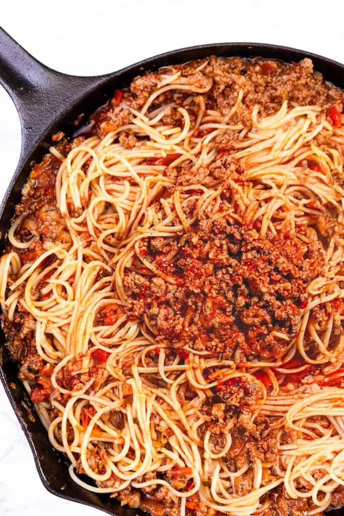 A close-up of a skillet filled with Quick & Easy Spaghetti Bolognese. The noodles are intertwined with ground meat, tomatoes, and spices, creating a rich, savory dish. The skillet's black edge frames the vibrant pasta meal.