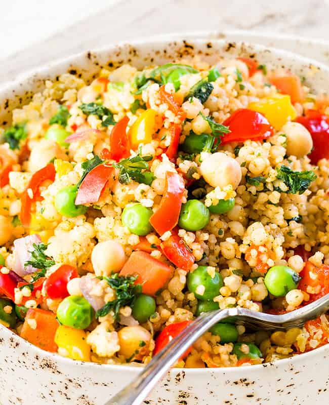 A close up image of Vegetable Moroccan Couscous in a bowl with a serving spoon.