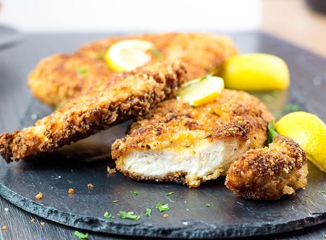 Crispy Breaded Chicken Cutlets on a dish with a piece cut off showing the juicy meat