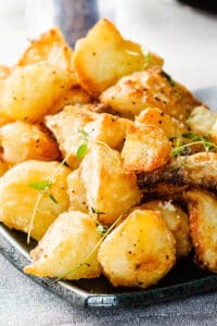 golden roasted potatoes piled high on a dish sprinkled with salt and fresh thyme