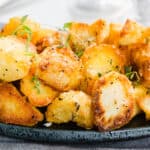 a close up image of Crispy Roasted Potatoes piled on a serving dish garnished with thyme