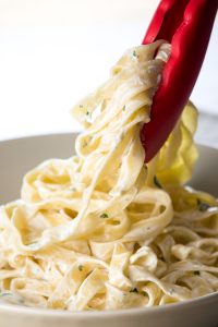 Fettuccine Alfredo being served into a bowl with tongs