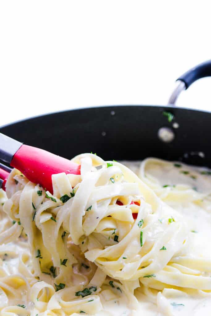 Fettuccine Alfredo being mixed in a pan with tongs