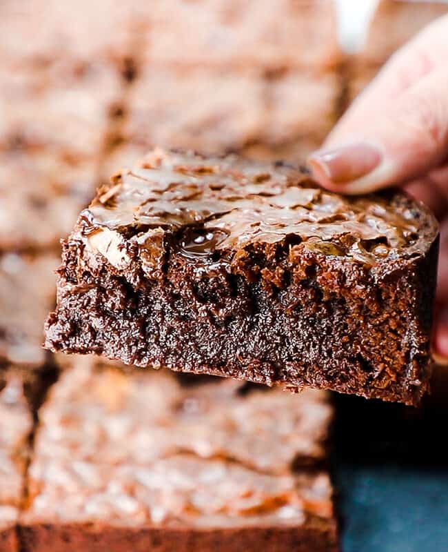 a woman's hand holding a fudgy brownie over a tray of Chocolate Chip Brownies