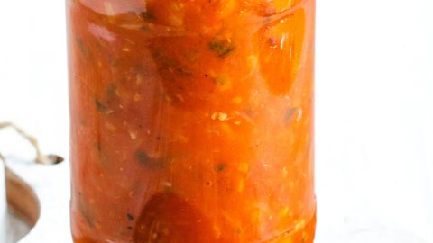 A jar of Tomato Sauce with basil and chopped parsley scattered around it