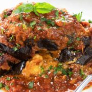 Baked Eggplant Parmesan on a white plate topped with fresh basil