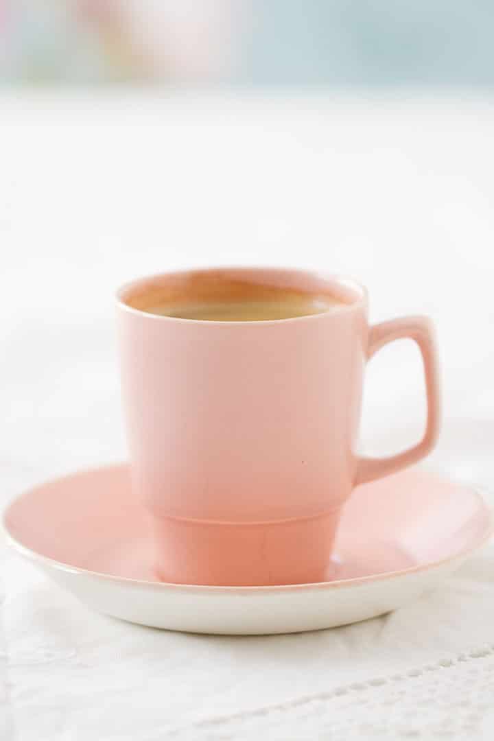 Espresso coffee in pink retro cup and saucer on a lacy white tablecloth against a fresh and floral background. 