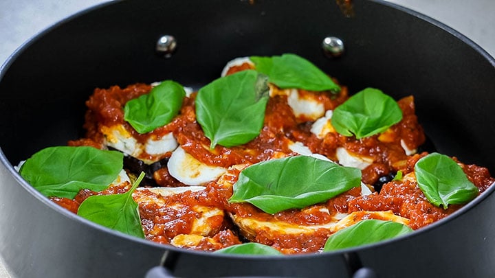 Basil leaves scattered across the top of the eggplant and tomato sauce