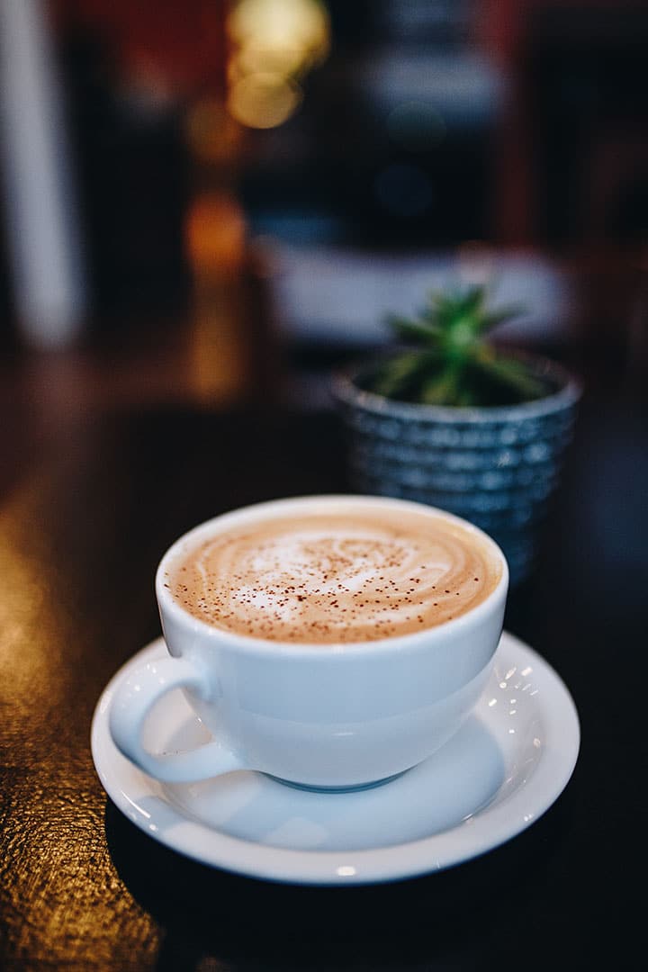 a white cup of cappuccino sprinkled with nutmeg on a dark table